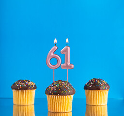Birthday candle with the number 61 - Three cupcakes on a blue background.