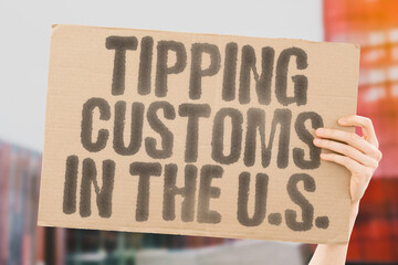"Tipping customs in the U.S." on worn cardboard. Highlights societal norms around service gratuities. ETIQUETTE. EXPECTATIONS. NORMS. PRACTICES. PAY. COMPENSATION. GRATIFICATION