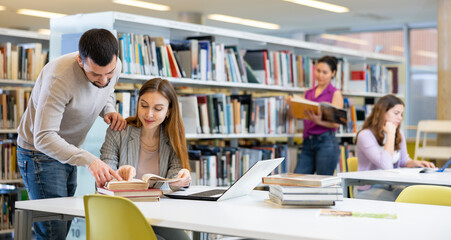 Male librarian helping focused adult student preparing to exam, bringing him books