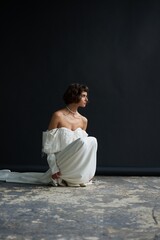 Fototapeta premium Model poses gracefully in elegant white dress against dark backdrop in a minimalist studio setting during late afternoon