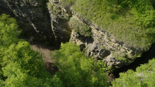 Scenic aerial view of Maltas Canyon, Dagestan, highlighting lush greenery, alpine trees, a mountain river, and cloud shadows drifting across the rugged landscape.