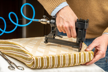 Close-up of an upholsterer’s hands upholstering a chair seat stapling fabric with a pneumatic...