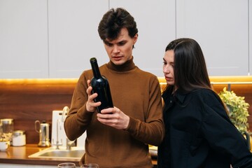 Young couple examining a wine bottle in a modern kitchen during evening