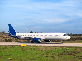 White and blue passenger aircraft on runway with grassy field and blue sky in background