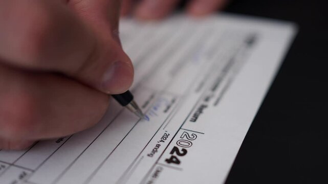 Man Filling In The Tax Form 1040 for 2024 Year. Person Calculates of Planning Budgets Yearly Personal Finance and Fills up US Tax Form 1040 For 2024 Year. Signing 1040 Income Tax Return For 2024 Year.