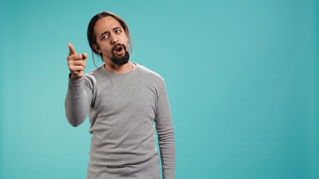 Angry man fighting with friend over debacle, putting blame on him, isolated over studio background. Rude person in disagreement with mate, swearing and pointing finger, camera B