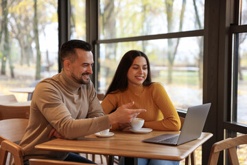 Colleagues with laptop working together at table in cafe