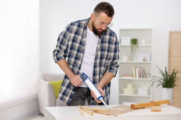 Man with caulking gun glueing plywood indoors