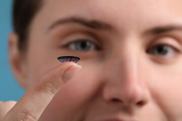 Woman with color contact lens on light blue background, closeup. Selective focus