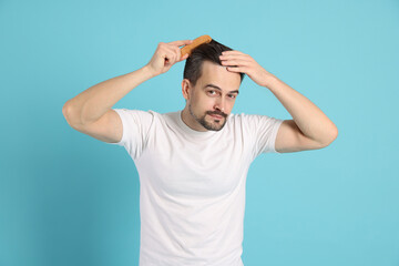Fototapeta premium Handsome man stylish his hair with comb on light blue background