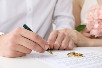 Newlyweds signing marriage contract and wedding rings on desk, selective focus