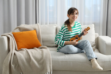 Happy woman playing ukulele on sofa at home