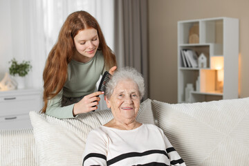 Obraz premium Granddaughter brushing her grandmother with comb at home