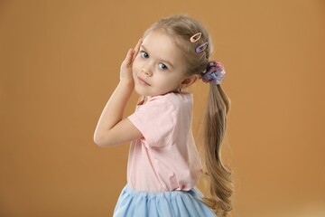 Cute little girl wearing beautiful hair accessories on light brown background