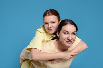 Fototapeta premium Portrait of beautiful mother with teenage daughter on light blue background