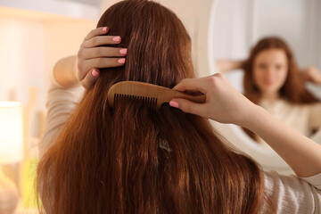 Naklejka premium Teenage girl brushing her hair with comb near mirror at home, selective focus