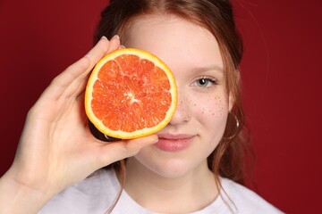 Beautiful teenage girl with freckles holding grapefruit slice on red background, closeup