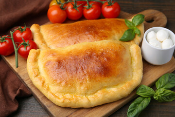 Tasty vegetarian calzones with basil, mozzarella cheese and tomatoes on wooden table, closeup