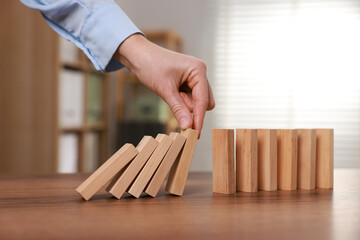 Woman stopping wooden blocks from falling at table, closeup. Domino effect