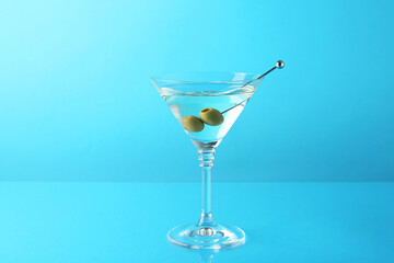 Martini cocktail with olives in glass on light blue background