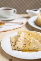 Tasty crepes with honey on wooden table, closeup