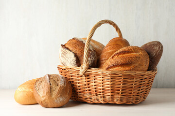 Different freshly baked bread loafs and wicker basket on white wooden table