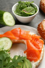 Delicious bagel with salmon, cream cheese, cucumber and avocado on grey table, closeup
