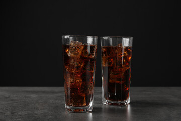 Cold cola with ice cubes in glasses on grey table against black background