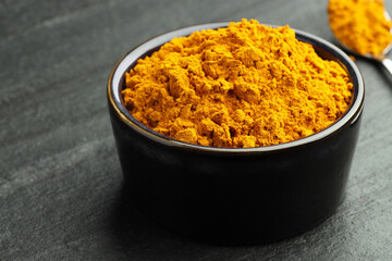 Turmeric powder in bowl on grey table, closeup