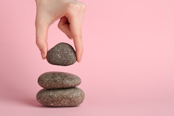 Woman making stack of stones on light pink background, closeup. Harmony and life balance