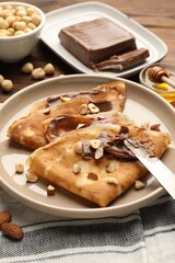 Tasty crepes with chocolate butter, nuts, honey and knife on table, closeup