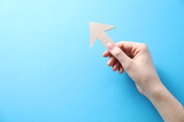 Woman with paper arrow on light blue background, top view. Space for text
