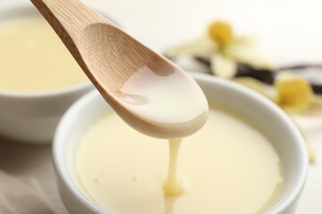 Taking tasty vanilla condensed milk with spoon from bowl on white table, closeup