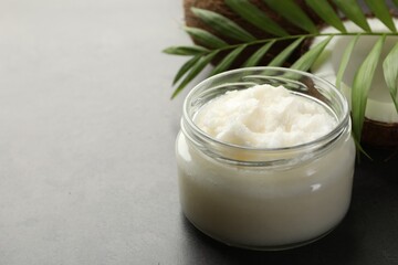 Organic coconut cooking oil in jar, fresh fruits and green branch on grey table, closeup. Space for...