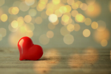 Fototapeta premium Valentine's day greeting card. Small red heart on wooden table against blurred lights, bokeh effect. Space for text