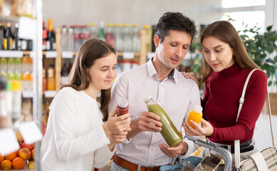 Positive family with teenage girl choosing a bottle of smoothie in grocery store