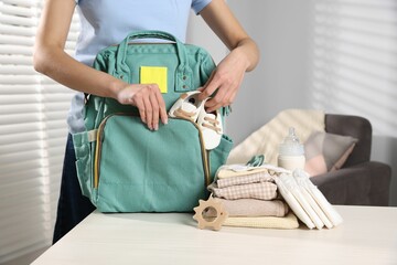 Mother packing baby's stuff into bag at white table, closeup