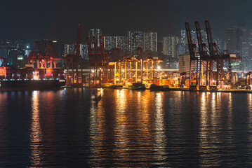 Hong Kong, China - night in the port container terminal, lights over the cranes, ships and containers, reflections on the water. 