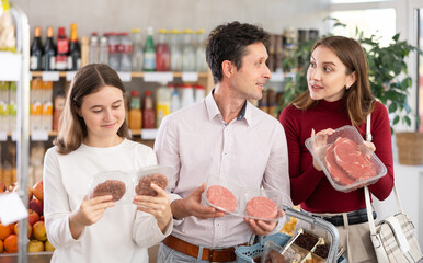 Couple adult man and young woman with teenage daughter buy hamburger patty or beef entrecote in grocery store
