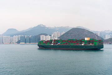 Large fully loaded container ship sailing near Hong Kong Island on her way to the port terminal.