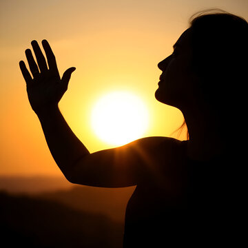 Silhouette of beautiful young gracile pensive woman with a freedom feeling  rise hand up on beautiful sunset. Freedom and travel adventure happy feeling concept.
