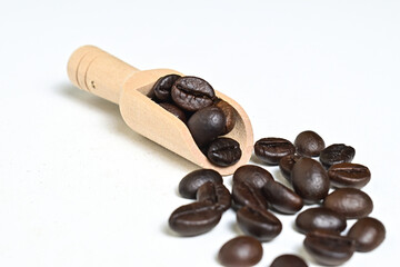 Obraz premium Close up view of roasted coffee beans in little wooden scoop with roasted coffee beans around it isolated on white background. Clipping path.