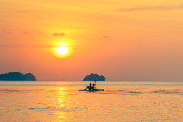 Man and woman enjoying colorful sunset at sea on SUP board on a summer evening