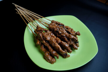 Satay or Sate is a popular Indonesian dish consisting of skewered and grilled meat, usually served with peanut sauce or sweet soy sauce. Served on a green plate isolated on a black bacground