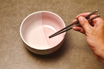 Hand Holding Metal Chopsticks Against a Neutral Background