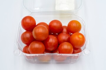 Fresh cherry tomatoes in a plastic container on a white background