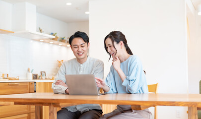 自宅のリビングでパソコンを見るアジア人のカップル