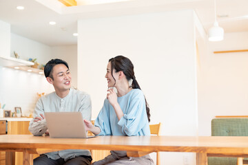 自宅のリビングでパソコンを見るアジア人のカップル