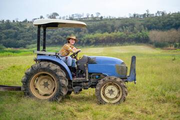 White woman sitting on tractor at grass field with smile. Female farmer with agricultural equipment...