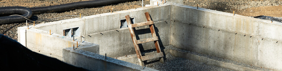 New housing build construction site, poured cement foundation gravel fill and wood ladder to enter and exit, sunny winter day, housing growth and development
